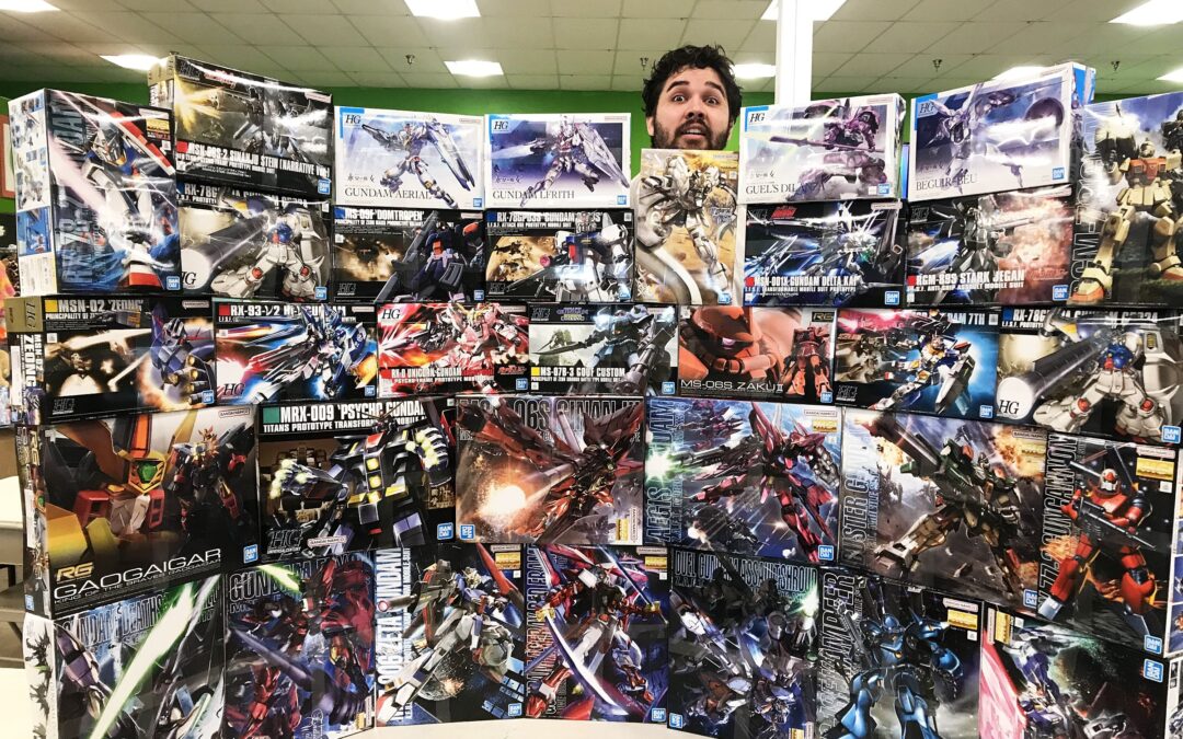 Wall of Gundam unopened Gundam boxes stacked into a wall shape with a man peeking out from behind it