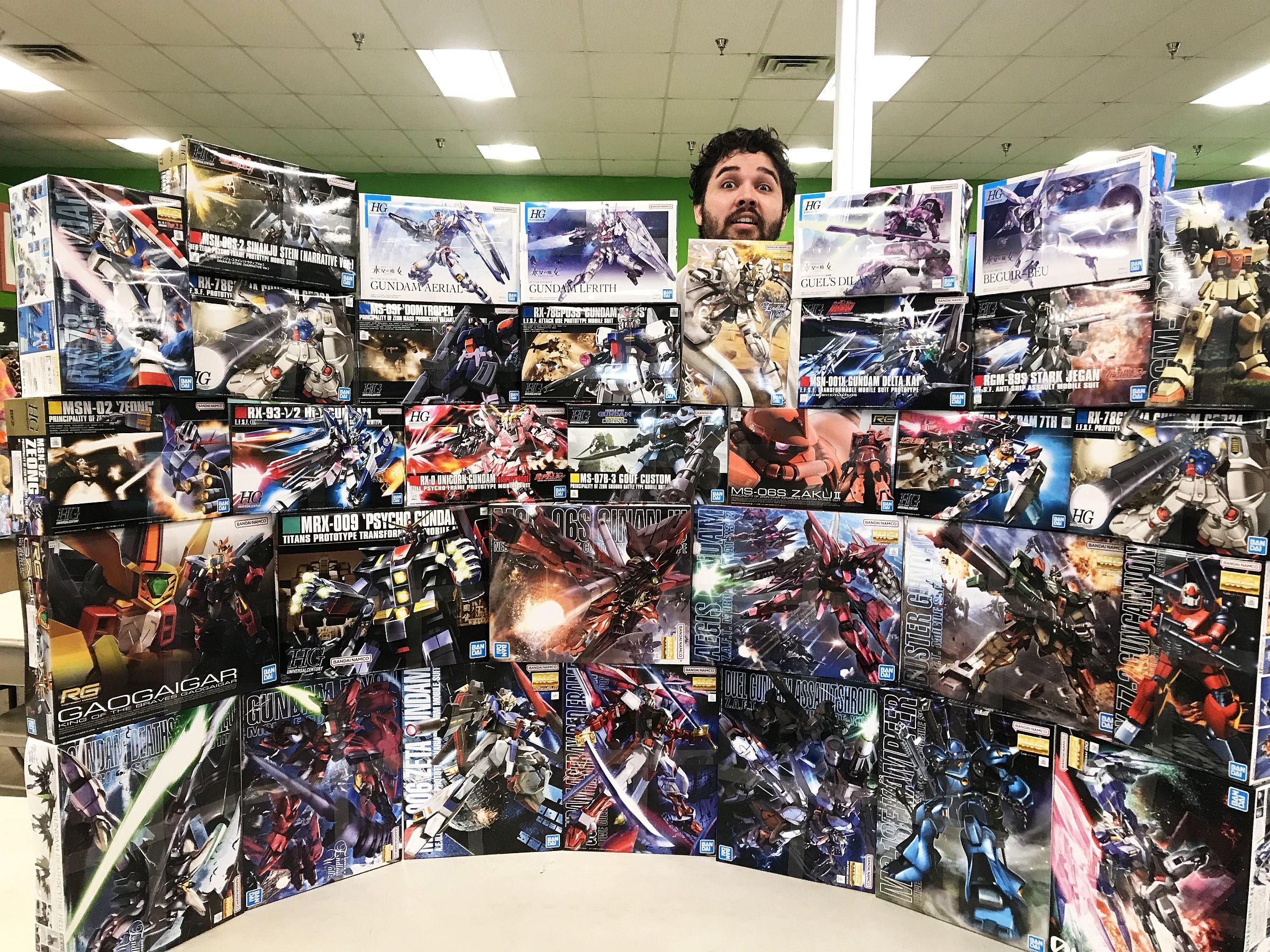 Wall of Gundam unopened Gundam boxes stacked into a wall shape with a man peeking out from behind it