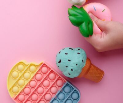 a child's hand squeezing a foam pineapple with a foam ice cream cone and sensory pop toy nearby