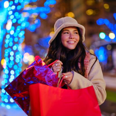 a girl in a puffer jacket and bucket hat holding holiday shopping bags