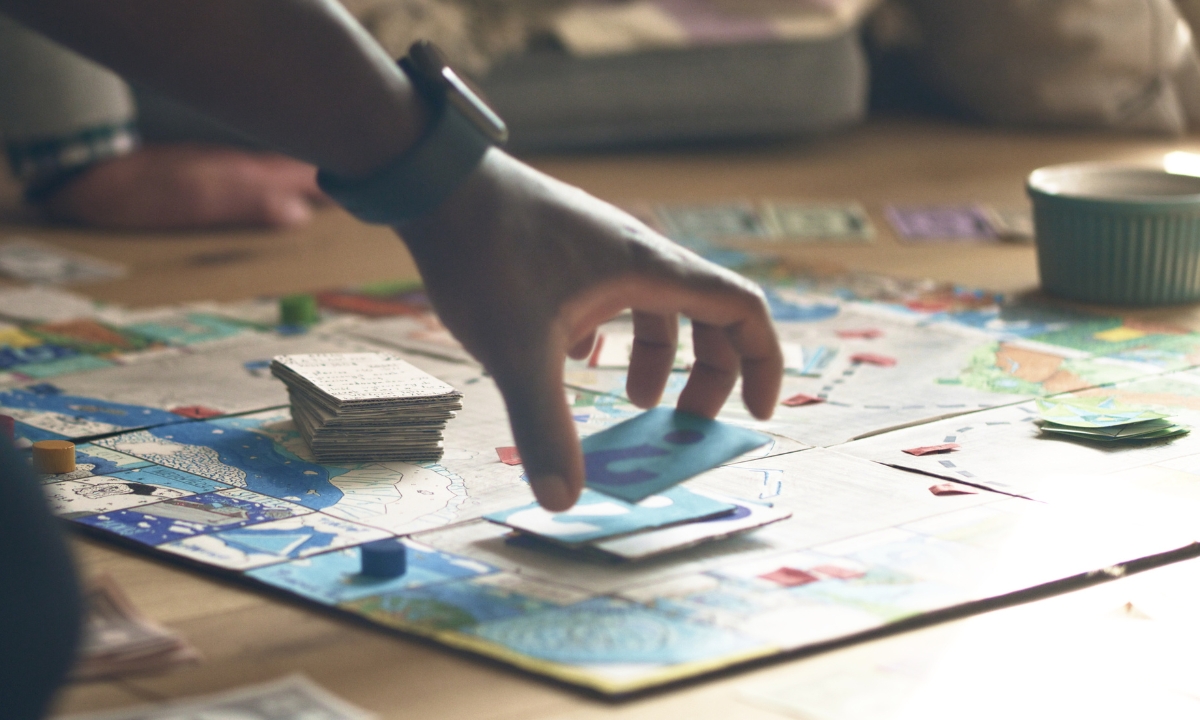 a board game on the floor with a person's hand reaching for a card